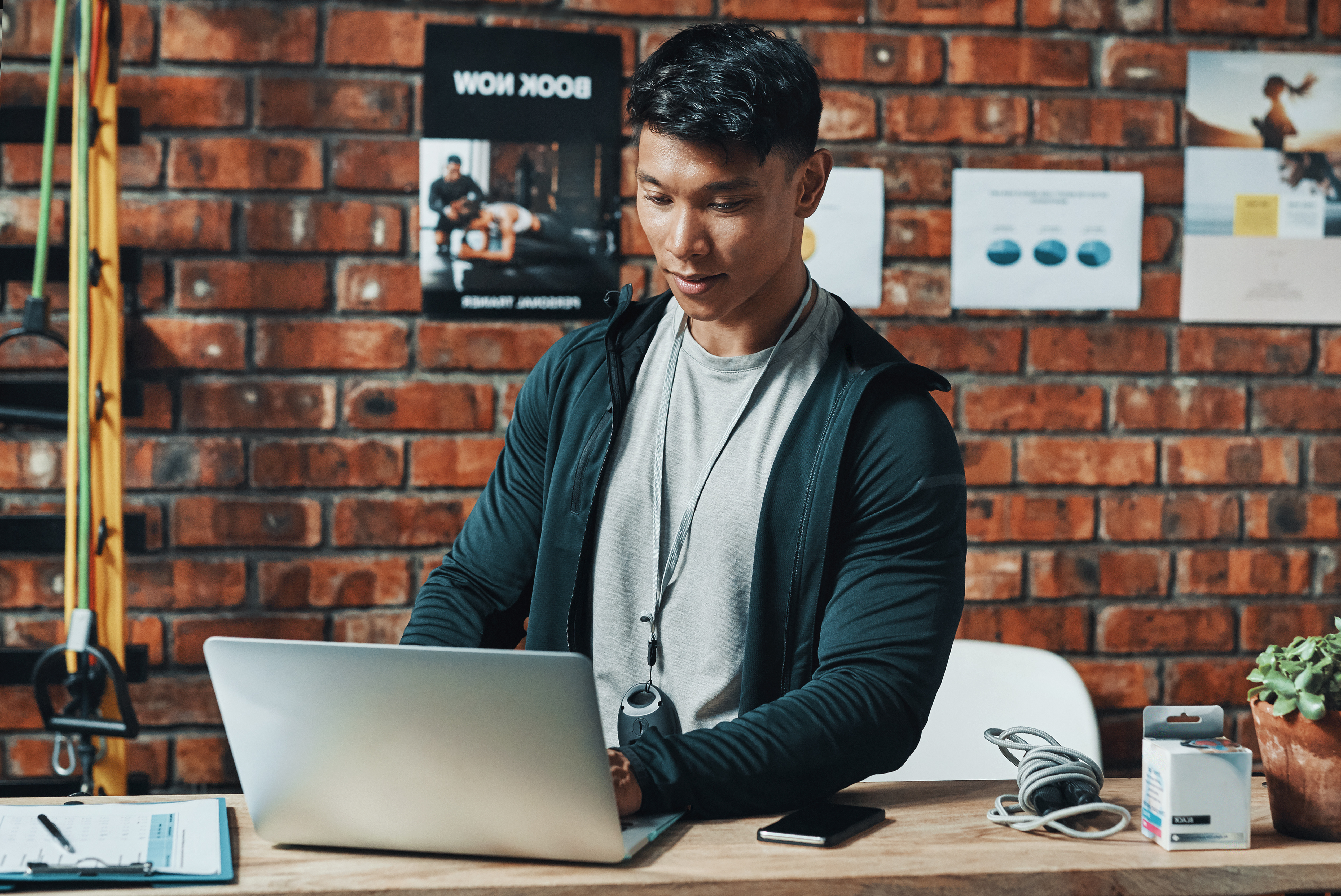 Trainer sitzt am Schreibtisch im Studio und arbeitet konzentriert am Laptop